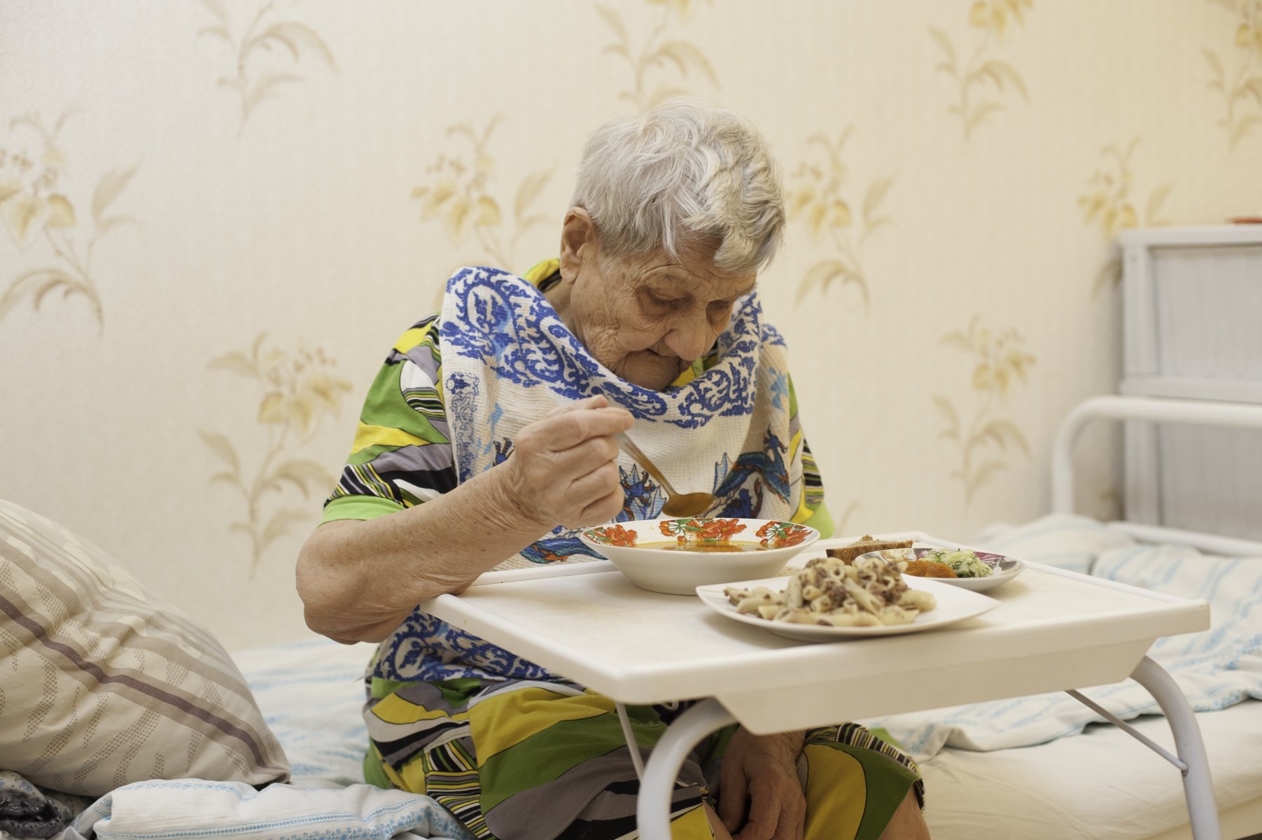 В скромно обставленном кабинете сидел пожилой человек. Пища для пожилых людей. Бабушка за столом. Питание в доме престарелых. Столик для пожилых людей.